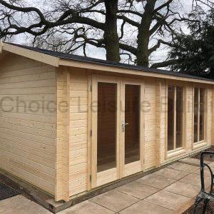 A wooden summerhouse with double doors and large windows, surrounded by trees and plants.