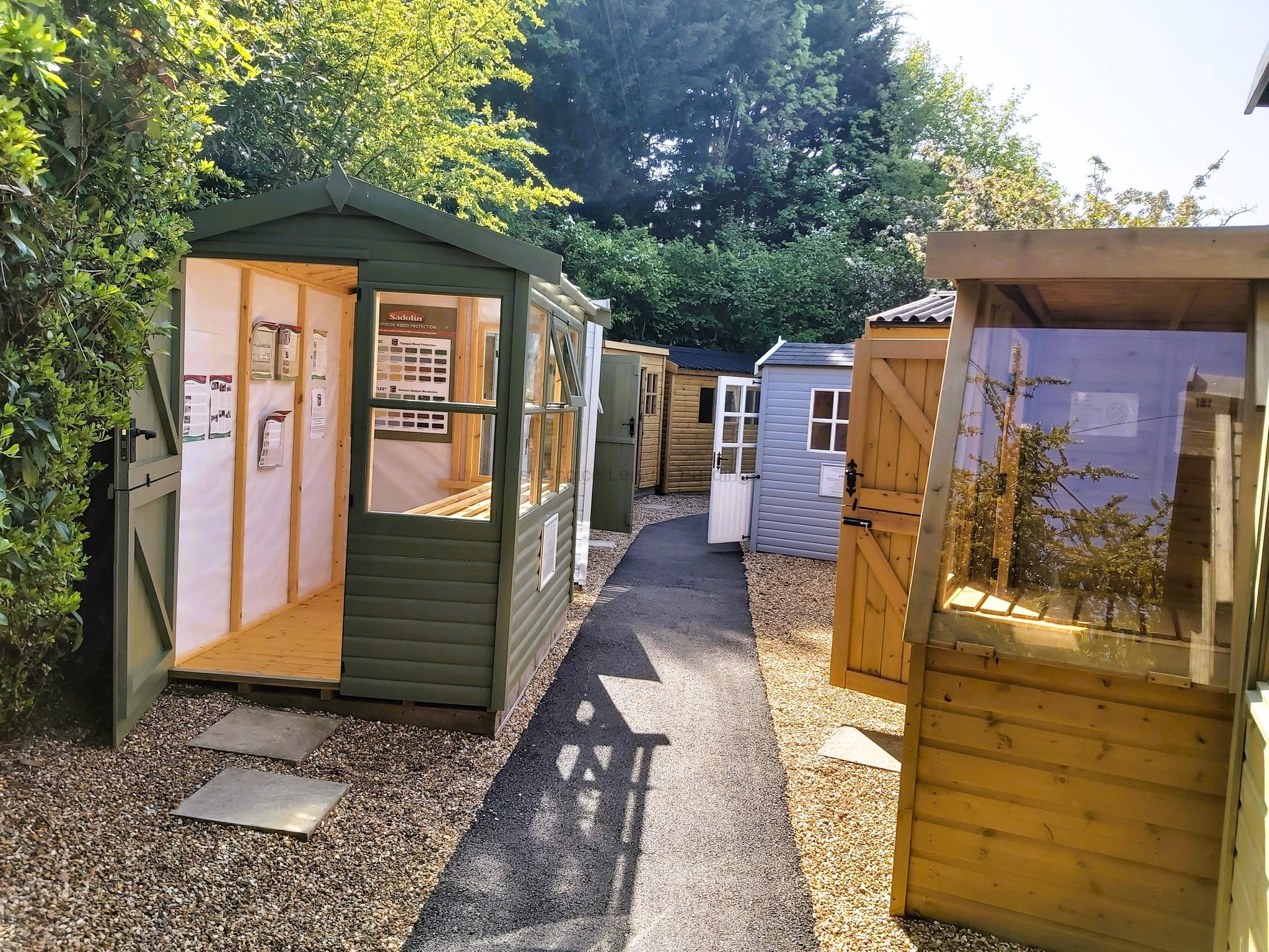 Garden sheds in various colours on show A row of wooden garden sheds in various colours. A green shed with its door open.