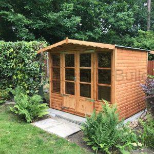 A wooden summerhouse with double doors and large windows, surrounded by trees and plants.