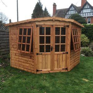 A wooden summerhouse with double doors and large windows, surrounded by trees and plants.