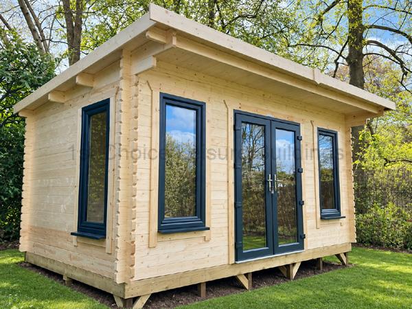 Pale timber garden cabin with charcoal-framed windows and glazed double doors, installed in a leafy garden.