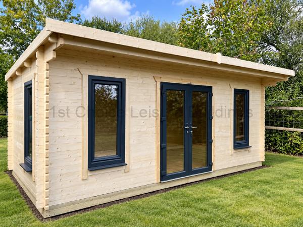Pale timber log cabin with charcoal-framed double doors and tall windows, installed in a tidy green garden.