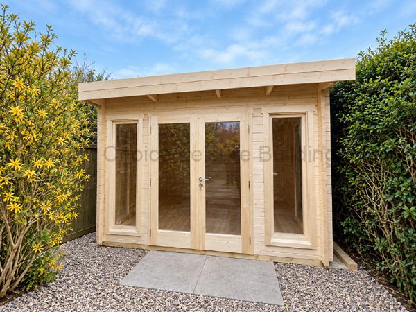Small wooden log cabin with glass-panel doors in a shingle garden, bordered by plants.
